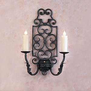 A decorative wall sconce featuring intricate wrought iron scrollwork and two candle holders. The fixture showcases a rich, dark finish and elegant curves, perfect for adding warmth and charm to any space.