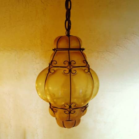 A beautifully designed hanging light fixture featuring a bulbous, amber glass shade wrapped in intricate wrought iron detailing, perfect for adding warmth to any space.