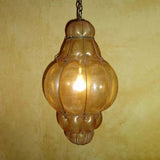 A decorative pendant light featuring a textured, amber glass shade encased in wrought iron, suspended from a chain against a warm, earthy wall.