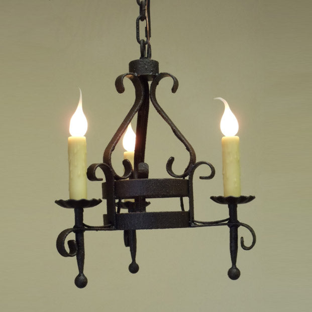 A decorative chandelier featuring intricate wrought iron design with three candle-like lights. The piece combines elegance and rustic charm, enhancing interior spaces with its unique style and character.