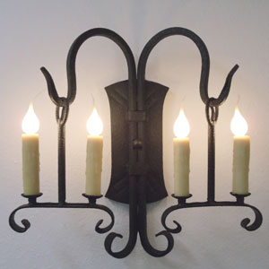 A decorative wall sconce featuring four candle-style lights in a classic wrought iron design. The elegant curves and intricate details enhance any room's ambiance.