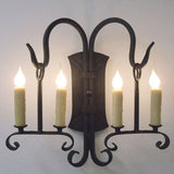 A decorative wall sconce featuring four candle-style lights in a classic wrought iron design. The elegant curves and intricate details enhance any room's ambiance.