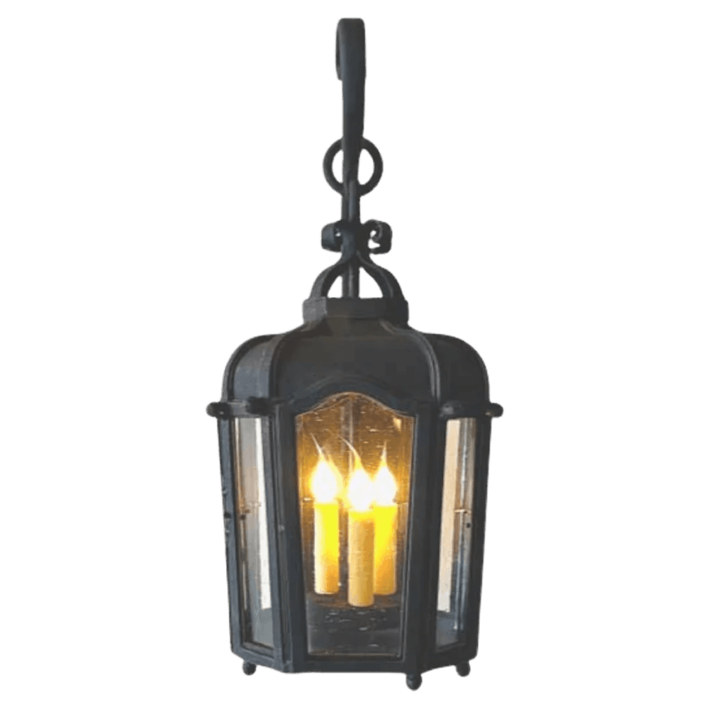 A beautifully crafted wrought iron pendant features a classic lantern shape with elegant curves. It showcases three candle-style lights within a glass enclosure, casting a warm glow. The fixture is suspended from a decorative hook, adding character and charm.