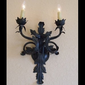 A beautifully crafted wall sconce featuring intricate leaf and flower designs, with two elegant candle-shaped bulbs illuminating the space. The wrought iron construction adds a touch of timeless charm.