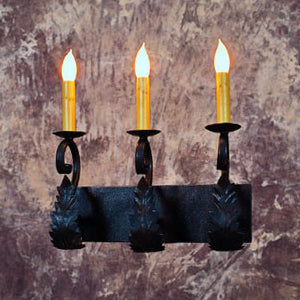 A dark wrought iron wall sconce featuring three elegant candle-style lights. The design incorporates intricate leaf details and curved elements, enhancing its rustic charm.