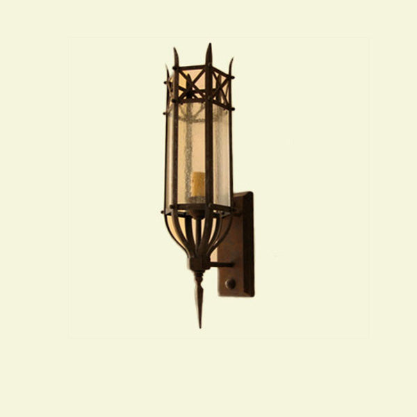 A detailed wrought iron wall sconce featuring a cylindrical glass shade with a textured finish and a decorative top. The design incorporates pointed accents and an elegant base, blending functionality with artistic flair. Ideal for adding charm to various interior spaces.